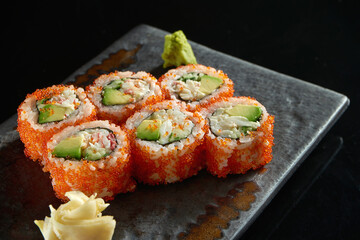 California sushi roll with crab, avocado, cucumber and tobiko caviar served on a plate with wasabi and ginger. Isolation on a black background. Japanese food