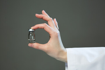 Vial of medicine or vaccine in doctor hand, close up on gray background. Vaccination and healthcare