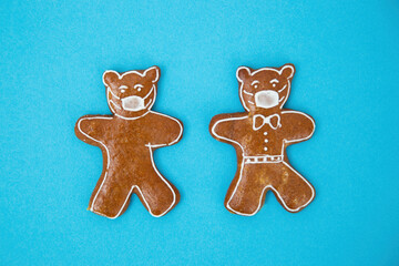 Two gingerbreads with face mask from sugar icing on blue background. Christmas cookies with surgical mask lying on turquoise table. Traditional biscuit with coronavirus symbol.