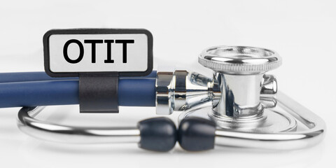 On the white surface lies a stethoscope with a plate with the inscription - OTIT