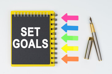 On a white background lies a pen, arrows and a notebook with the inscription - SET GOALS