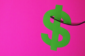 Obraz premium A green dollar sign is placed on a fork on a pink background with a copy space. Conceptual collage about currency in the style of minimalism. High quality photo