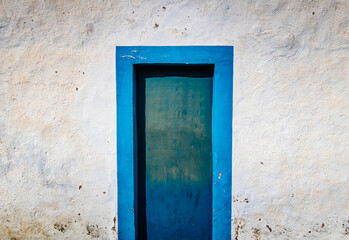 Metal door with a blue painted border on the wall, on a weathered white facade, with a rustic touch. Typical Mediterranean style. 