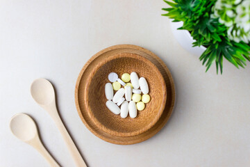 Obraz na płótnie Canvas A handful of pills in a wooden plate with spoons and green plant. The concept of medcine, treatment. Top view.