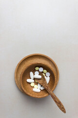 A handful of pills in a wooden plate with spoon. The concept of medcine, treatment. Top view. Vertical photo