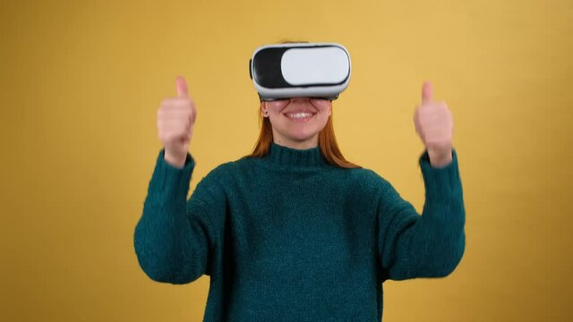 Young woman using VR app headset helmet. Isolated on yellow background in studio