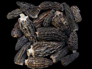 dried morel mushrooms lie in a bunch isolated on black background