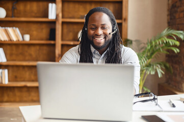 Front view on African-American guy using a laptop and hands free device for online communication...