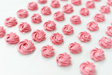 Photo of a group of pink cute meringue sweets on a white table.