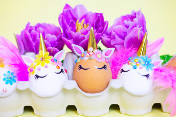 white Easter eggs decorated in the form of unicorns on a colorful background with ranunculus flowers, a minimal creative concept of a happy Easter
