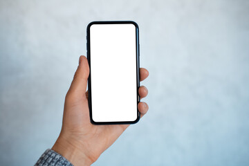Close-up portrait of male hand, holding a smartphone with mockup, on the background of light grey wall.