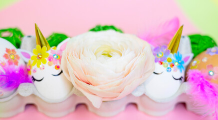 white Easter eggs decorated in the form of unicorns on a colorful background with ranunculus flowers, a minimal creative concept of a happy Easter