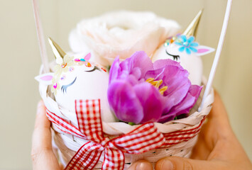 white Easter eggs decorated in the form of unicorns and flowers in basket in boy's hands, a minimal creative concept of a happy Easter