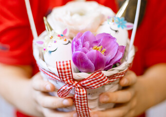 Easter eggs decorated in the form of unicorns and flowers in basket in boy's hands, a minimal creative concept of a happy Easter
