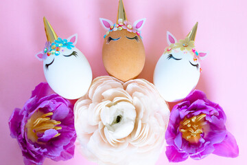 white and brown Easter eggs decorated in the form of unicorns on a pink background with ranunculus and tulips flowers, a minimal creative concept of a happy Easter