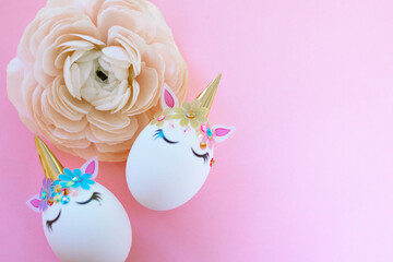 Easter eggs decorated in the form of unicorns on a pink background with ranunculus flower, a minimal creative concept of a happy Easter