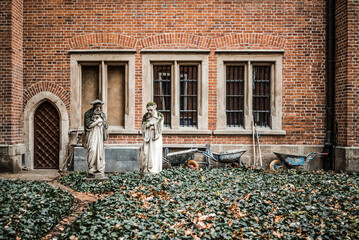 Abandoned old stone religious statues outside empty building being renovated with wheel barrows and over grown garden looking sad and lost outdoors left behind