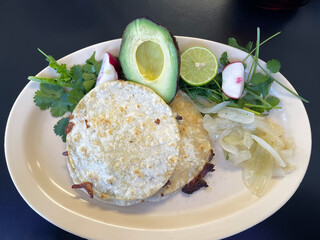 A plate of food consisting of steak and cheese quesadillas, half of an avocado, grilled onions, and garnishes of cilantro, lime, and radishes.