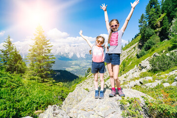 Children hiking on beautiful summer day in alps mountains Austria, resting on rock and admire...