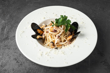 Spaghetti with seafood and parmesan on a white plate and dark concrete background