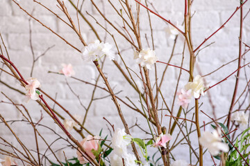 Decorations of branches with beautiful pink and white flowers in the basket against the background of a white brick wall