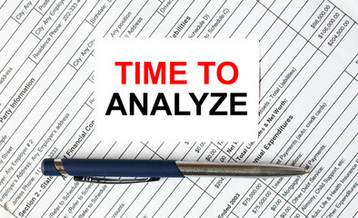 Text Time To Analyze written on a business card lying on financial tables with a blue metal pen