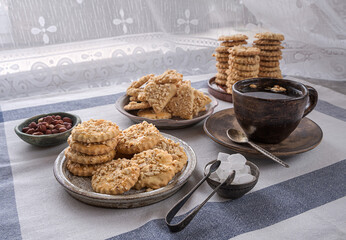 Three ceramic plates of shortbread peanut cookies, a cup of herbal tea, a bowl of white sugar, and a saucepan of peanuts sit on a linen napkin. The concept of home-made food.