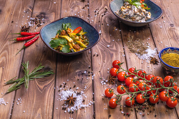 Vegetable salads in plates, cherry tomatoes, cinnamon, rosemary on a brown wooden background.