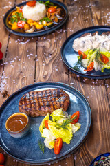 Fototapeta na wymiar Steak with sauce, lettuce, rosemary, cherry tomatoes on a wooden board. Flat layout.