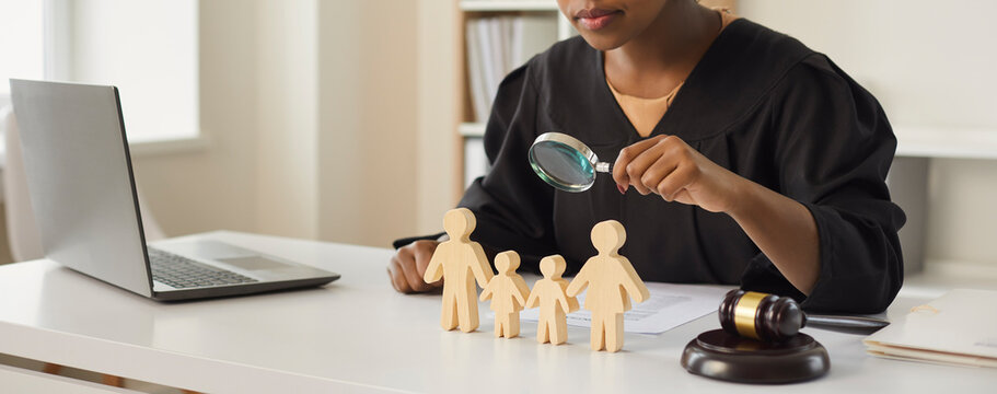 African american judge looking through magnifying glass at wood family figure making decision on children custody. Parental rights deprivation law and guardianship concept. Cropped portrait