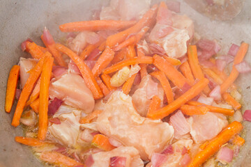 Chicken pieces are fried with carrots and red onions in a cauldron on the grill