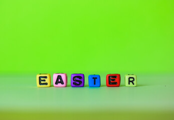 Easter word written with multicolored wooden alphabet letters on a bright green background. Minimalistic Easter background. Greeting card for Christian or Catholic Easter. Place for text flatly