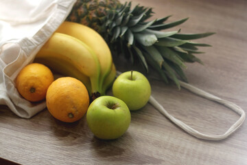 Linen tote bag with pineapple, bananas, lemons and apples. Selective focus.