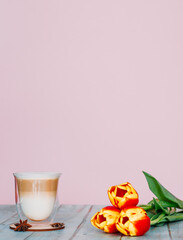 Gentle still life with a transparent cup of cappuccino or latte and star anise on a wooden background. Beautiful delicate pink background. Women's holiday concept