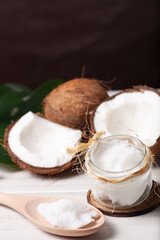 Fototapeta na wymiar Bodegón de dos cocos, uno de ellos cortado por la mitad, con un tarro de aceite de coco sobre un fondo marrón oscuro.