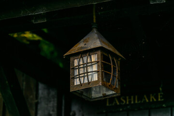 Single vintage lantern hanging over the door to old english cottage house, rusty old electric lamp in shape of a small house hanged above the entrance to a country house.
