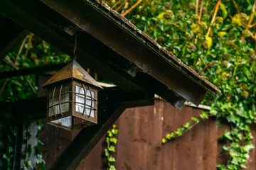 Single vintage lantern hanging over the door to old english cottage house, rusty old electric lamp in shape of a small house hanged above the entrance to a country house.