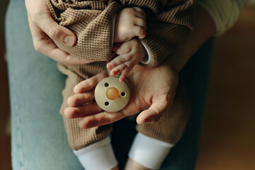 baby holds a pacifier in his mother arms