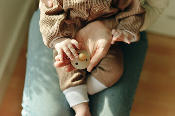baby holds a pacifier in his mother arms