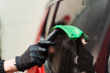 Removal of residual water from the glass with a rubber scraper after washing the car. Car Wash. Self-service complex. High-pressure car wash.