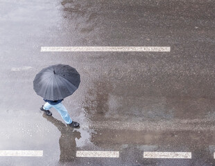 A man walks on the road with a black umbrella in the rain. Top view