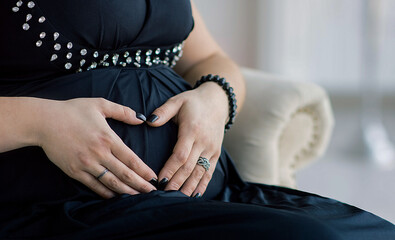 hands female embrace a pregnant belly and show the heart