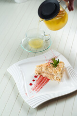 Napoleon cake decorated with a spiral of red chocolate, mint and berry jam on a white plate against a background of orange tea in a teapot and a transparent cup. Layered cake with pastry cream.
