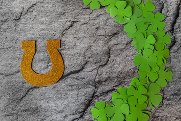 side frame made of clover leaves, next to it lies a horseshoe cut out of paper on a gray background