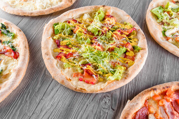 Assortment of pizza with meat, salami, prosciutto, tomatoes, dorblu cheese, mozzarella, parmesan, salad, spinach, red fish on wooden boards. Four cheese pizza, caesar, top view.