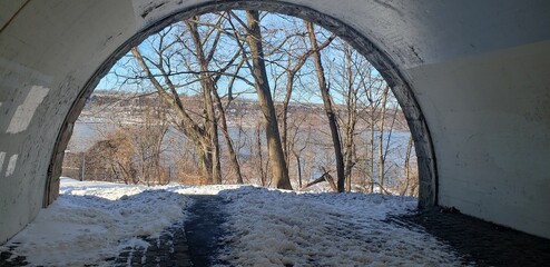 View looking out of an underpass tunnel in Inwood Hill toward the Hudson River on a snowy, winter...