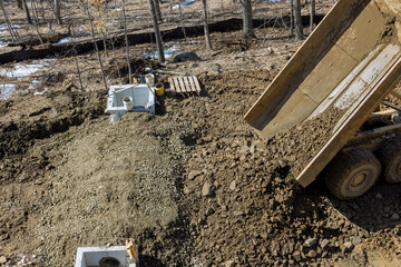 Dump truck dumps its load of rock and soil on road construction site the installed water drainage...