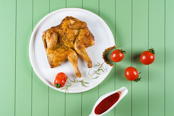 Chicken tobacco with tomato sauce, rosemary and tomatoes on a beautiful white plate on a green...