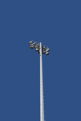 Low angle view of a single very tall mast with sports stadium lights and a bright blue sky behind