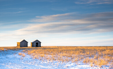 Two old vintage farm sheds sit on a winter harvested field on the Canadian prairies in Rocky View...